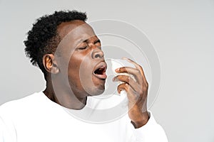 Black man blowing nose and sneeze into tissue or napkin, has allergy, first symptoms of cold and flu