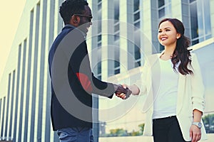 Black man and Caucasian female handshake over modern building.