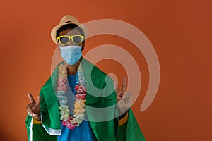 Black man in costume for carnival with brazil flag and pandemic mask isolated on orange background. African man in various poses