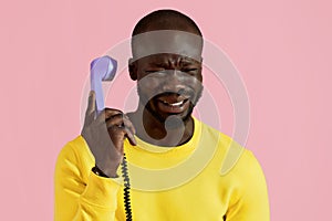 Black man crying, talking on phone on pink background portrait