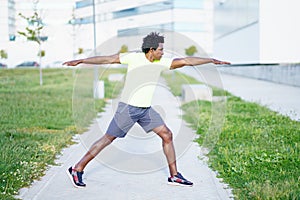 Black man doing Warrior 2 or Virabhadrasana II pose outdoors.