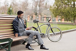 Black man in earphone sitting on bench listening to radio