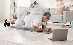 Black Man Exercising Doing Plank Exercise At Laptop Indoors