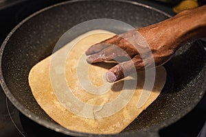 Black man frying flat bread at home. Flat bread with on the frying pan. Fresh multi-grain tortillas photo
