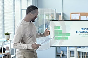 Black man giving presentation in office standing by digital screen