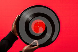 Black man hand holding old vinyl retro record. Vinyl gramophone record on red background.