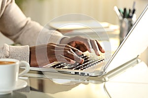 Black man hands typing on a laptop on a desk at home