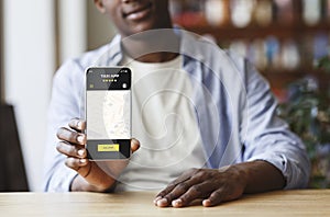 Black man holding smartphone with opened taxi services mobile app on screen