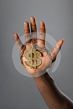 Black man holding up a gold Dollar symbol on a necklace