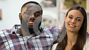 Black man looking at his pretty girlfriend, couple sitting on sofa and hugging