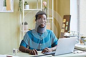 Black man with neck brace working at desk in office smiling at camera