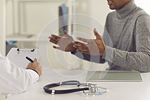 Black man patient sitting and explaining health complaints to man doctor photo