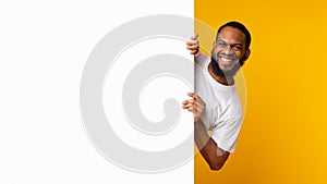 Black man peeking out blank white advertising billboard at studio