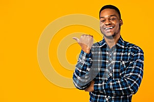 Black Man Pointing Thumb Aside Posing Over Yellow Studio Background