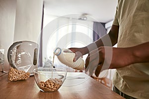 Black man pouring milk in bowl with cereals