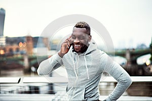 Black man runner with smartphone on the bridge in a city, making a phone call.