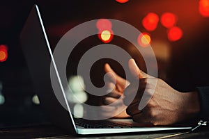 Black man's hands with thumbs up gesture. All is excellent. Person working on laptop. Beautiful lights as background