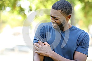 Black man scratching itchy arm in a park