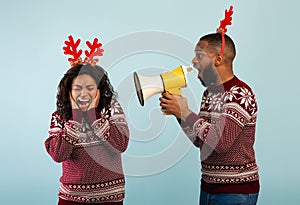 Black man shouting with megaphone loudspeaker at woman, standing together over blue background