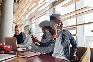 Black man sitting in front of group of multi ethnic people with alternative girl with green hair is working together by