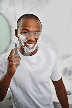 Black man, smile and shaving with blade, soap or grooming in mirror for self care in home bathroom. African guy, foam or