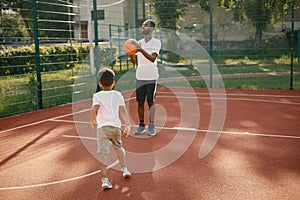 Black man with son playing basketball in basketball court together