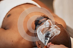 Black man spa, beauty skincare mask and lying relax for exfoliation on salon bed for cosmetic treatment. Man skin