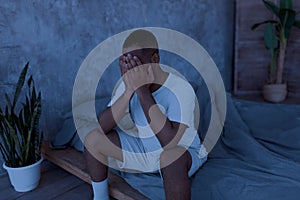 Black man suffering from insomnia sitting on bed