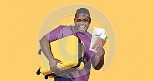 Black Man With Suitcase Showing Tickets Wearing Sunglasses, Yellow Background