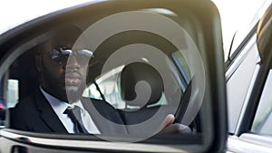 Black man in sunglasses driving car, looking in side-view mirror, bodyguard