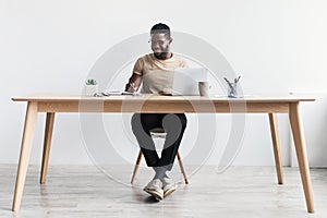 Black man taking notes during webinar or business meeting, using laptop, working or studying online, sitting at desk