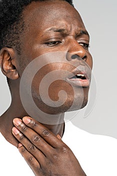 Black man touches fingers of sore throat, thyroid gland. Painful swallowing, tonsil, angina concept. photo