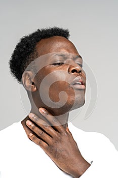 Black man touches fingers of sore throat, thyroid gland. Painful swallowing, tonsil, angina concept.