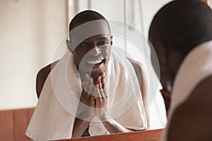 African man looking in mirror cleaning face after shaving