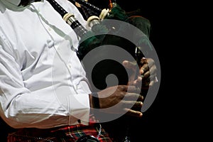 A black man in a white shirt is holding a Scottish bagpipe. Multicultural