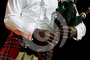 A black man in a white shirt and Scottish kilt holds bagpipes. Multicultural