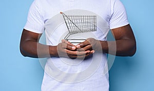 Black man with white t-shirt holds a shopping cart. cyan background