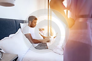 Black man and woman in the bedroom. A man is lying on the bed with laptop. Before him is his girl in lingerie.