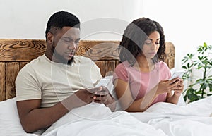 Black man and woman sitting in bed and using their smartphones