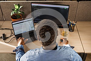 Black Man Writing Lines of Code On Desktop PC With Two Monitors and a Laptop Aside in Stylish Office. Professional Male