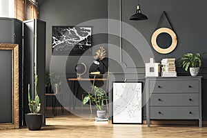 Black map on grey wall in dark living room interior with plants