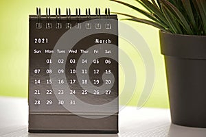 Black March 2021 calendar with green backgrounds and potted plant