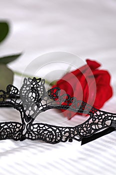 black mask for sex play and red rose lie on bed photo