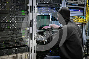 A black masked hacker hacks into the protection of the server room. Virus DDoS attack computer servers data center. Criminal