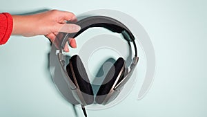 Black massive headphones in female hand on pastel background, copy space. Modern technology flat lay with over-ear earphones in