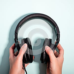 Black massive headphones in female hand on pastel background, copy space. Modern technology flat lay with over-ear earphones in