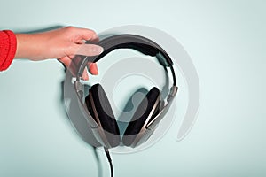 Black massive headphones in female hand on pastel background, copy space. Modern technology flat lay with over-ear earphones in