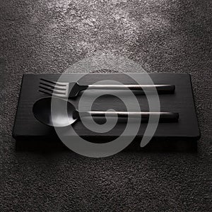 black matte fork with spoon close-up. on a dark background, modern tableware, square photo
