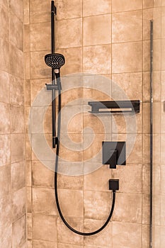 Black matte metal shower faucet on sand colored modern tiles, contemporary bathroom concept