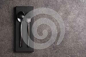 Black matte spoon and fork. Minimalistic set, copyspace for a restaurant or cafe menu against a dark concrete background